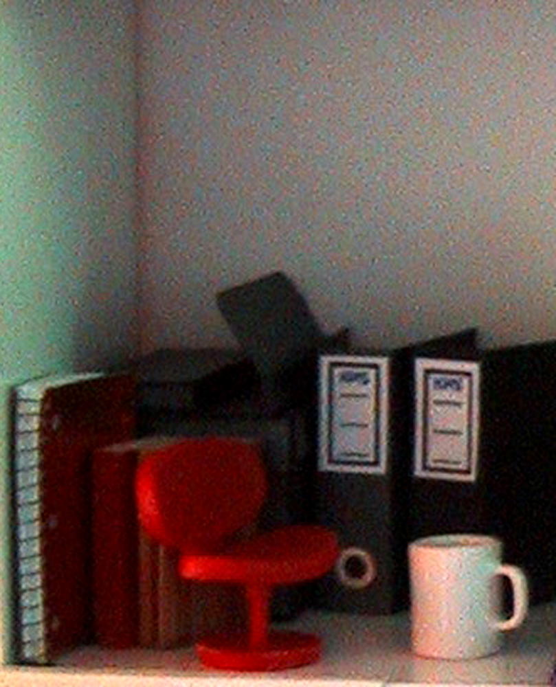 Modern dolls' house miniature desk corner with a spiral-bound notebook, ring binders, a model chair and a coffee mug.