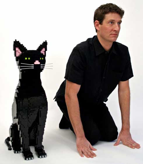 Large black cat made from Legos; man crouches beside it in the same pose